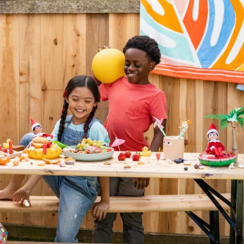 A boy and girl smile as they enjoy the summer picnic their Scout Elf has prepared for them