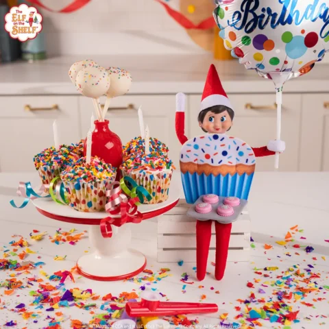 A girl Scout Elf dressed in a cupcake costume has prepared cupcakes and holds a birthday balloon