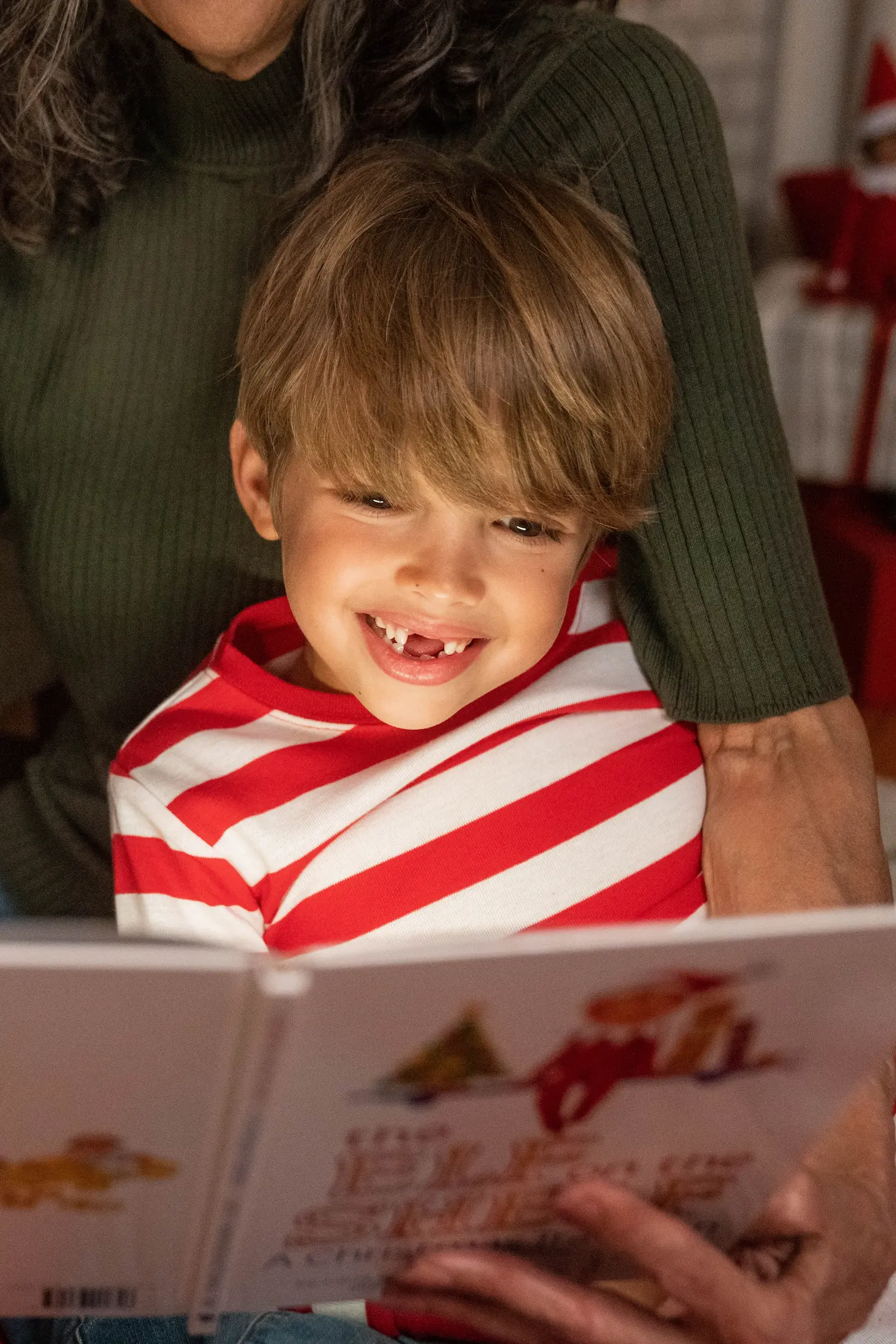 A boy missing his front teeth reads The Elf on the Shelf storybook