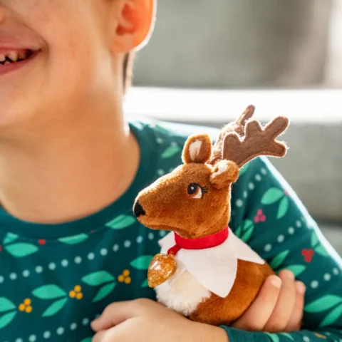 A young boy wearing green pajamas hugs his Elf Pets Reindeer