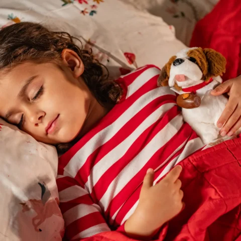 A girl in red and white striped pajamas sleeps with her Elf Pets Saint Bernard pup