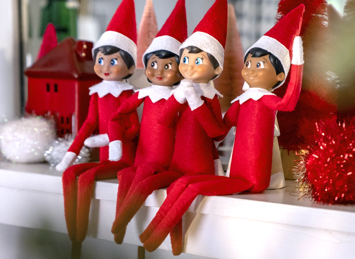 A grouping of Scout Elves sit atop a fireplace mantle. They are situated as a group hanging out and in different poses.