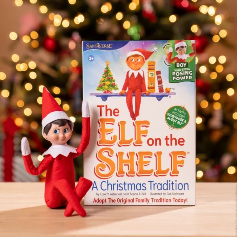 The Elf on the Shelf boxset with poseable Scout Elf on a wooden table with Christmas tree in background. 
