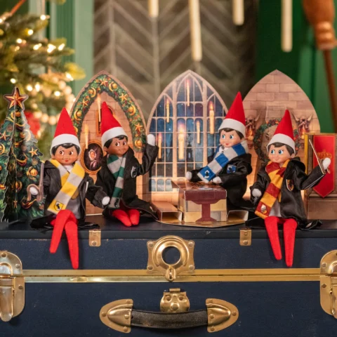 Four Scout Elves representing the Hogwarts Houses wear robes and scarves in front of a Great Hall-inspired scene