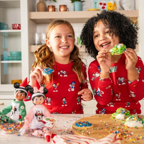 A boy and girl decorate cookies alongside their Scout Elf Girl and Scout Elf boy who are dressed in Mickey and Minnie pajamas