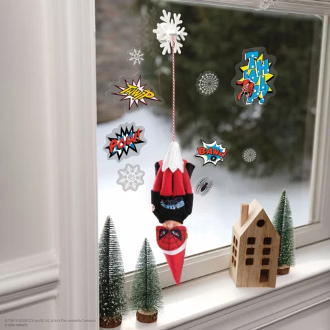 The Elf on the Shelf hangs upside down over a toy house and trees