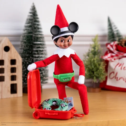 A girl Scout Elf wears a Mickey ears handband while packing a miniature suitcase
