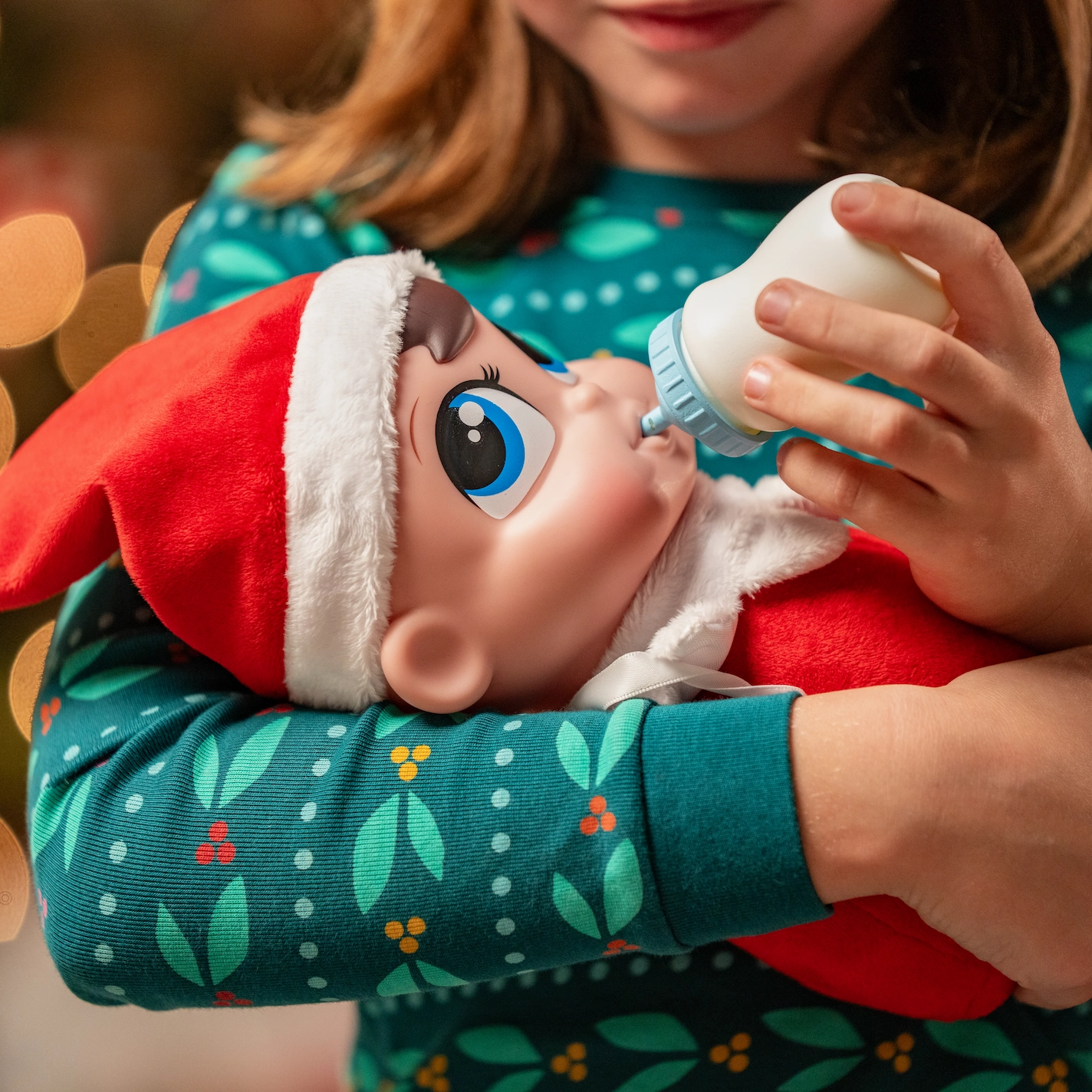 A young girl holds a bottle to feed the doll-sized Frost Pips elf baby