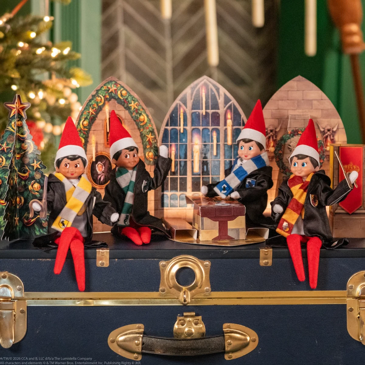 4 Scout Elves, each representing the four different Hogwarts Houses, wear Hogwarts robes and scarves in front of a Great Hall scene design