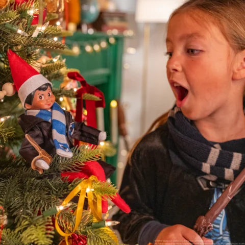 Scout Elf holds a miniature wand as young girls discovers elf in Christmas tree