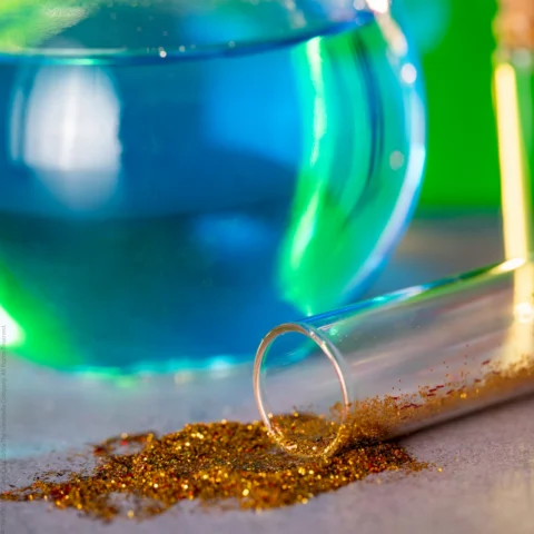 A glass jar of colored water and a container of glitter are used as supplies for a pretend potion