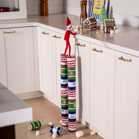 A Scout Elf uses stacked cans to reach the kitchen counter