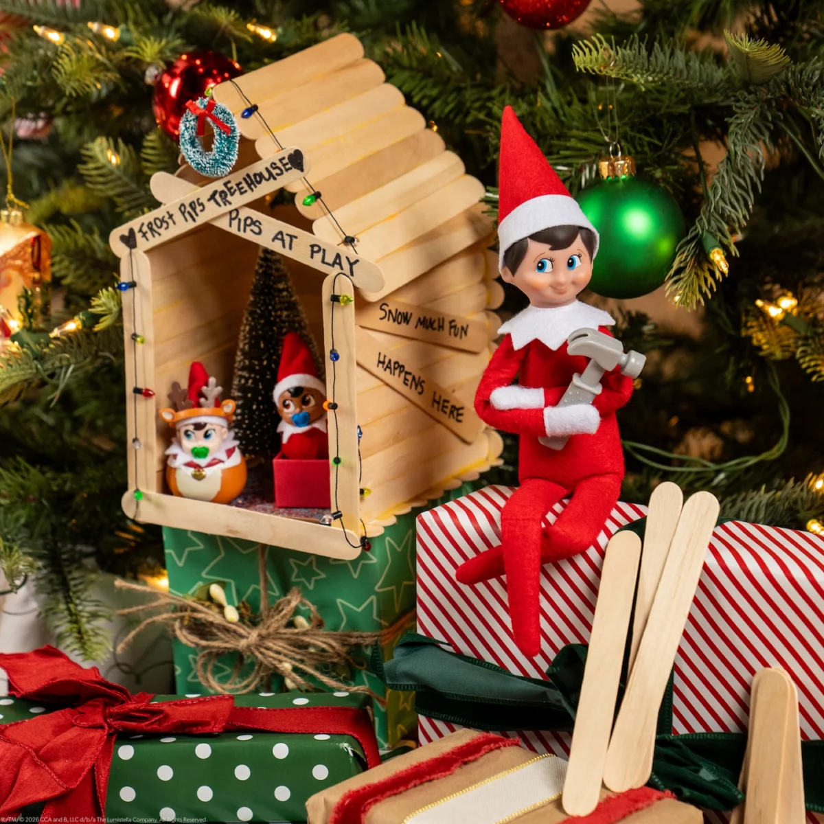 A Scout Elf sits beside a treehouse they made out of popsicle sticks for Frost Pips