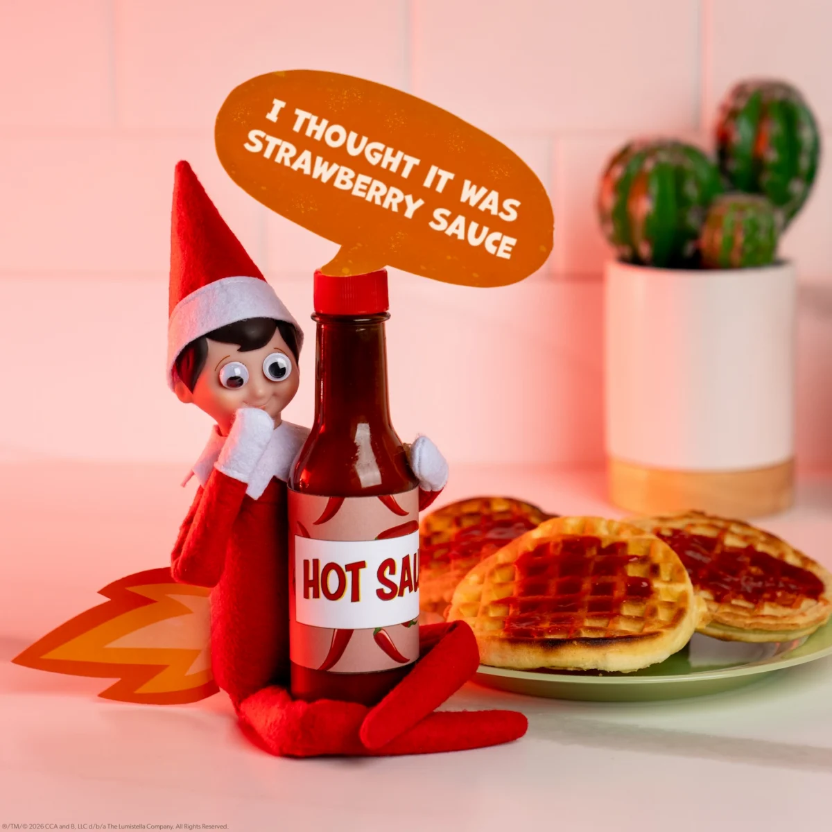 A Scout Elf with googly eyes over his eyes sits beside hot sauce with a sign saying he thought it was strawberry sauce