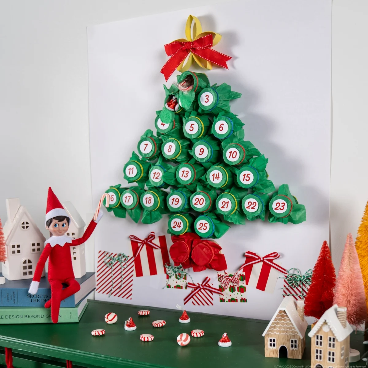 A Scout Elf sits beside a DIY advent calendar in the shape of a tree with 24 numbered sections