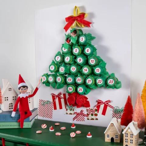 A Scout Elf sits beside a DIY advent calendar in the shape of a tree with 24 numbered sections