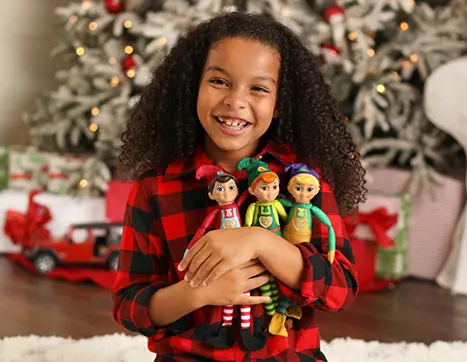 Girl hugging the three Elf Mates in front of a Christmas tree