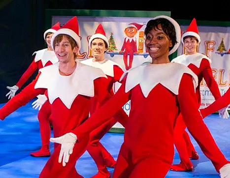 Several adults dressed as Scout Elves dancing on the stage during the The Elf on the Shelf musical production