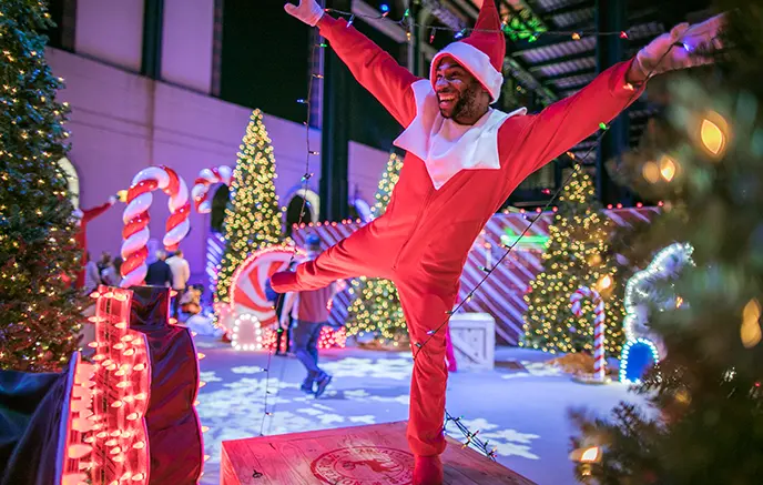 Man in a Scout Elf costume performing on top of a platform at the Elf on the Shelf’s Magical Holiday Journey