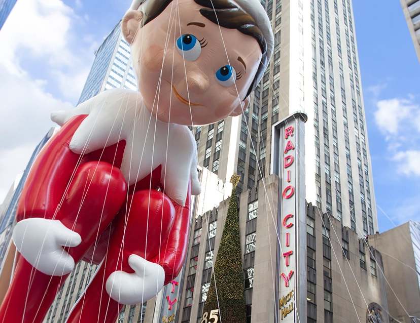 The Elf on the Shelf Macy's Day Thanksgiving Parade balloon floating past Radio City Music Hall