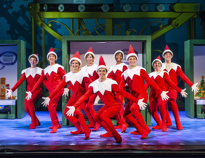 Adults dressed in Scout Elf costumes dancing on the stage during the The Elf on the Shelf musical production