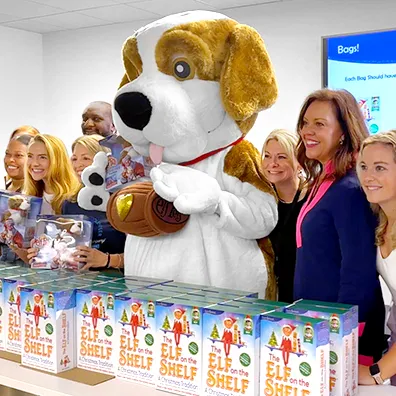 The Lumistella Company employees and a Saint Bernard mascot standing behind a table holding The Elf on the Shelf boxsets