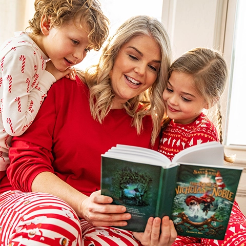 A mother and her children are sitting together in festive, Christmas pajamas. The children are fully engaged to their mother reading "The Rise of Nicholas the Noble" to them.