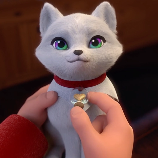 A close-up of an arctic fox cub being held on a boy's lap. The boy's left hand is holding the fox on her right shoulder, and holding the fox's snowglobe charm in his right hand.