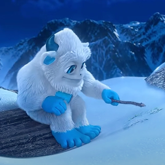 Little Grunt sitting on a log that's on a snowy hill with mountains in the background. He is drawing in the snow with a stick.