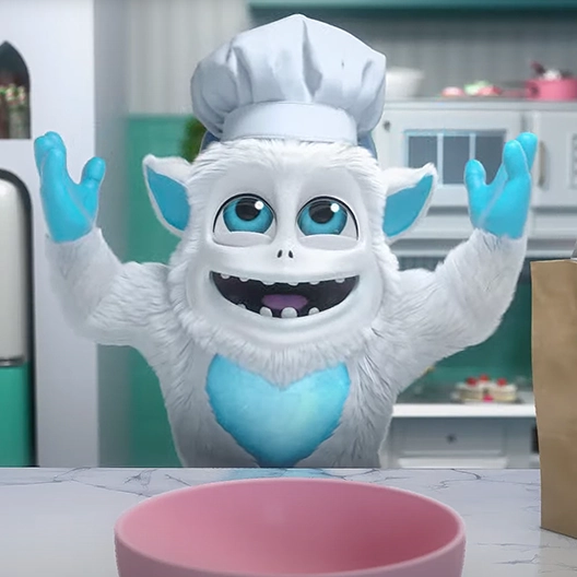 Little Grunt standing in front of a kitchen counter with a chef's hat on. He is smiling, has both hands raised up in the air, and is looking up. Behind him is a kitchen scene.