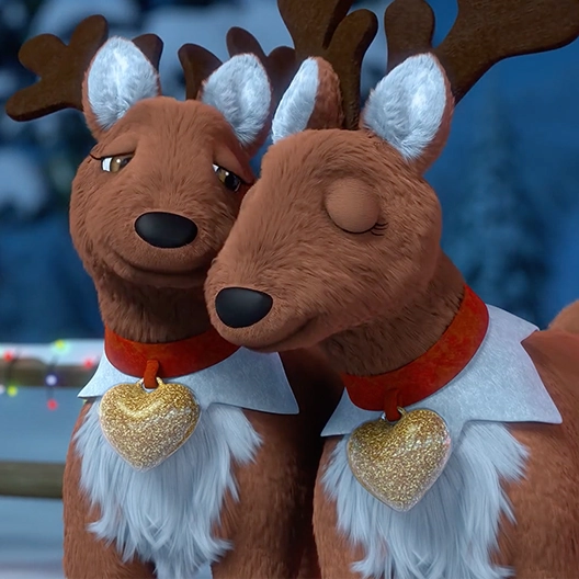 Two Elf Pets Reindeer from the chest up snuggling their faces together. The one on the right is looking down at the one on the right, and the one on the right has his eyes closed. Behind them are snow-covered pine trees and a wooden fence wrapped with Christmas lights.