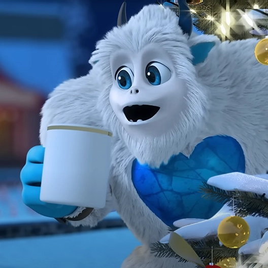 A Snobiggie Yeti peeking out from behind a Christmas Tree with a white and gold mug of hot cocoa in his hand.