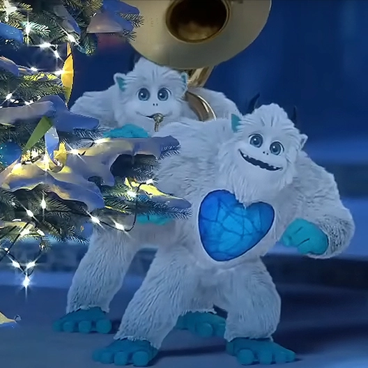 Two SnoBiggie Yetis leaning out from behind a Christmas Tree. One of the yetis is playing a tuba.