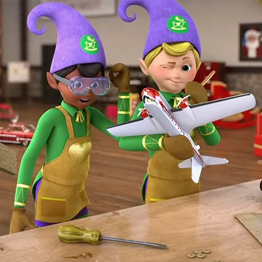 Two toy makers standing in front of a wooden counter top. One elf is painting a model airplane he is holding while the other looks down at the toy with joy and surprise.