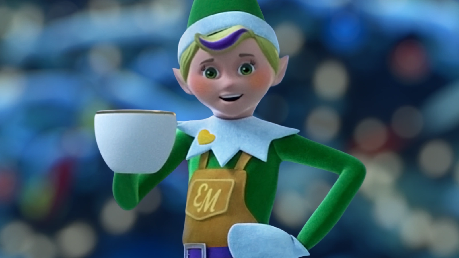 An Elf Mates Toy Maker is holding a mug of hot cocoa with his left hand placed on his hip. He has a smile on his face. In the background is a blurry Christmas tree.