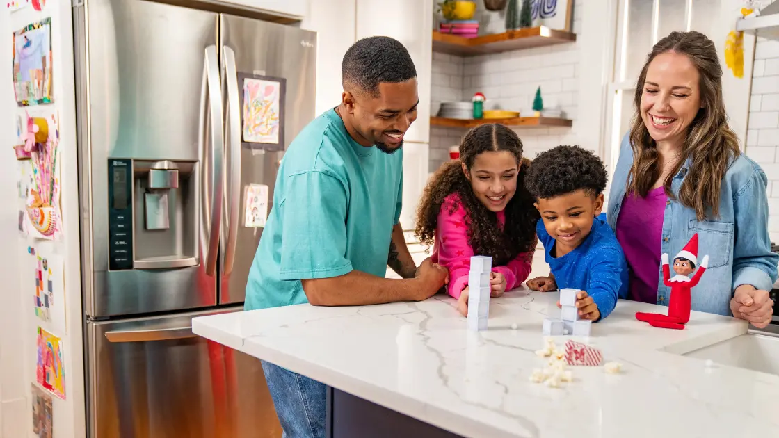 Familia de cuatro en la mesa de la cocina con el Elfo Explorador en el Estante