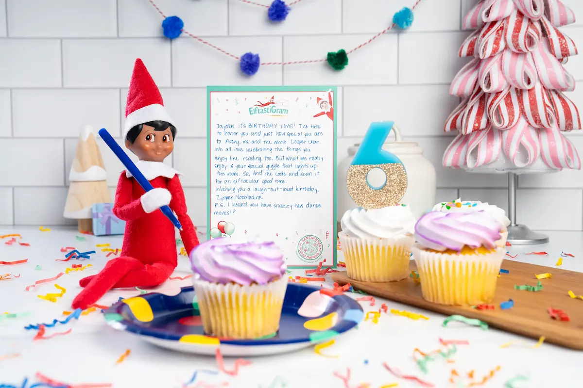 Elf Scout writing on notepad with cupcakes around on a kitchen counter.