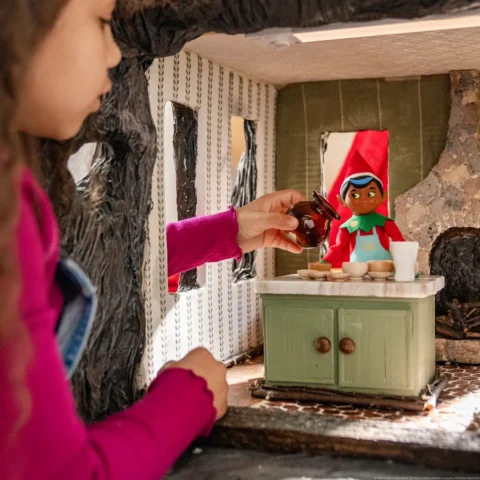 A child playing with an Elf Mates Chef figure in a wooden North Pole kitchen scene