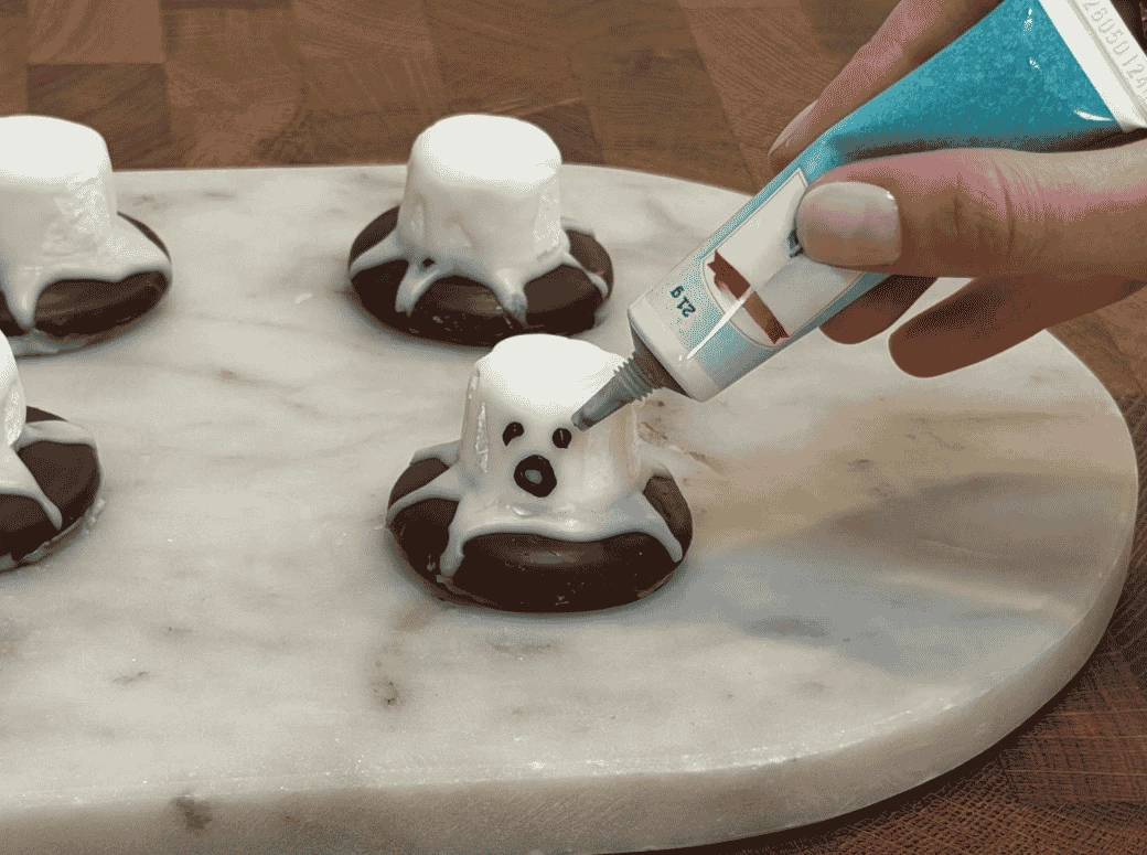 Faces being added to the ghost biscuits with black writing icing