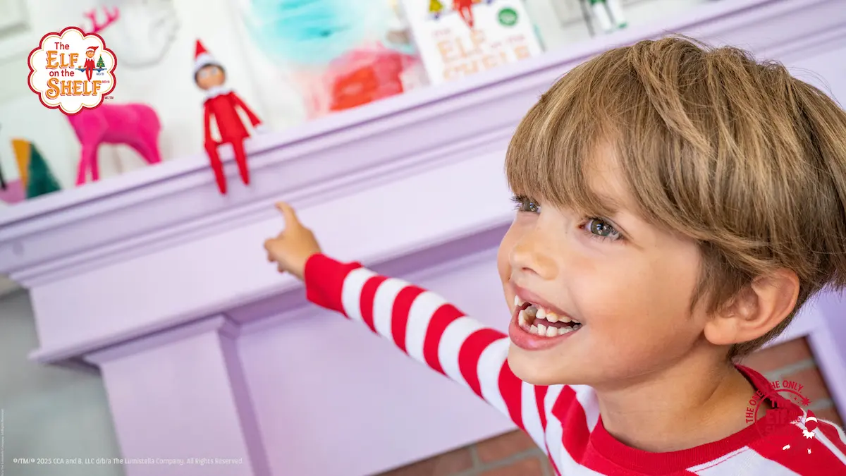 Elf on the Shelf on mantle with child in red white shirt pointing.