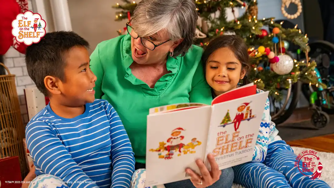 Grandmother and two children reading The Elf on the Shelf book in front of Christmas Tree