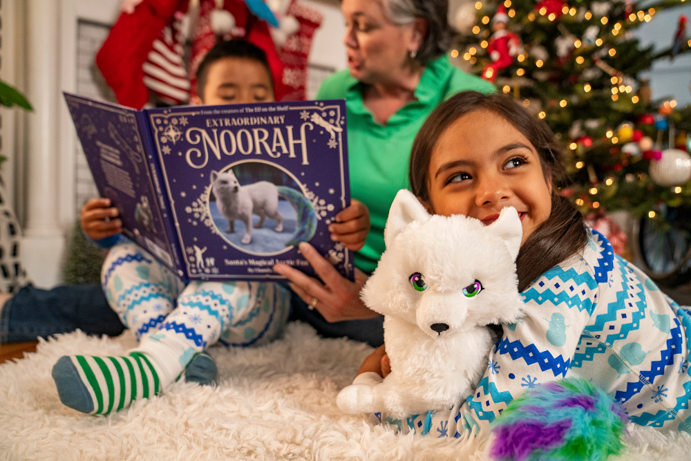 Family reading the Noorah book in front of christmas tree with Noorah plushie