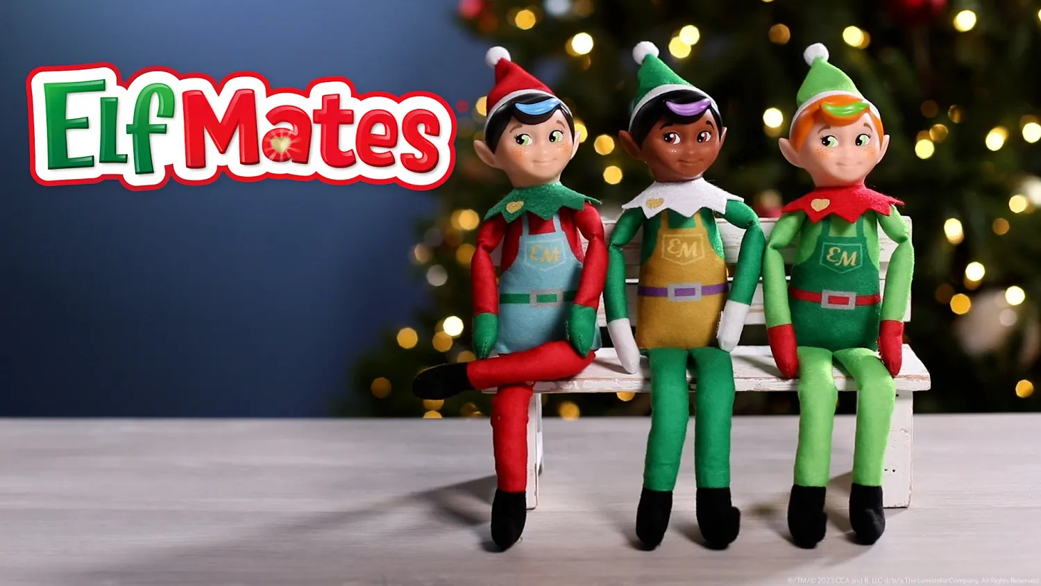 Elf Mates dolls sitting on a bench in front of a Christmas tree with festive lights in the background