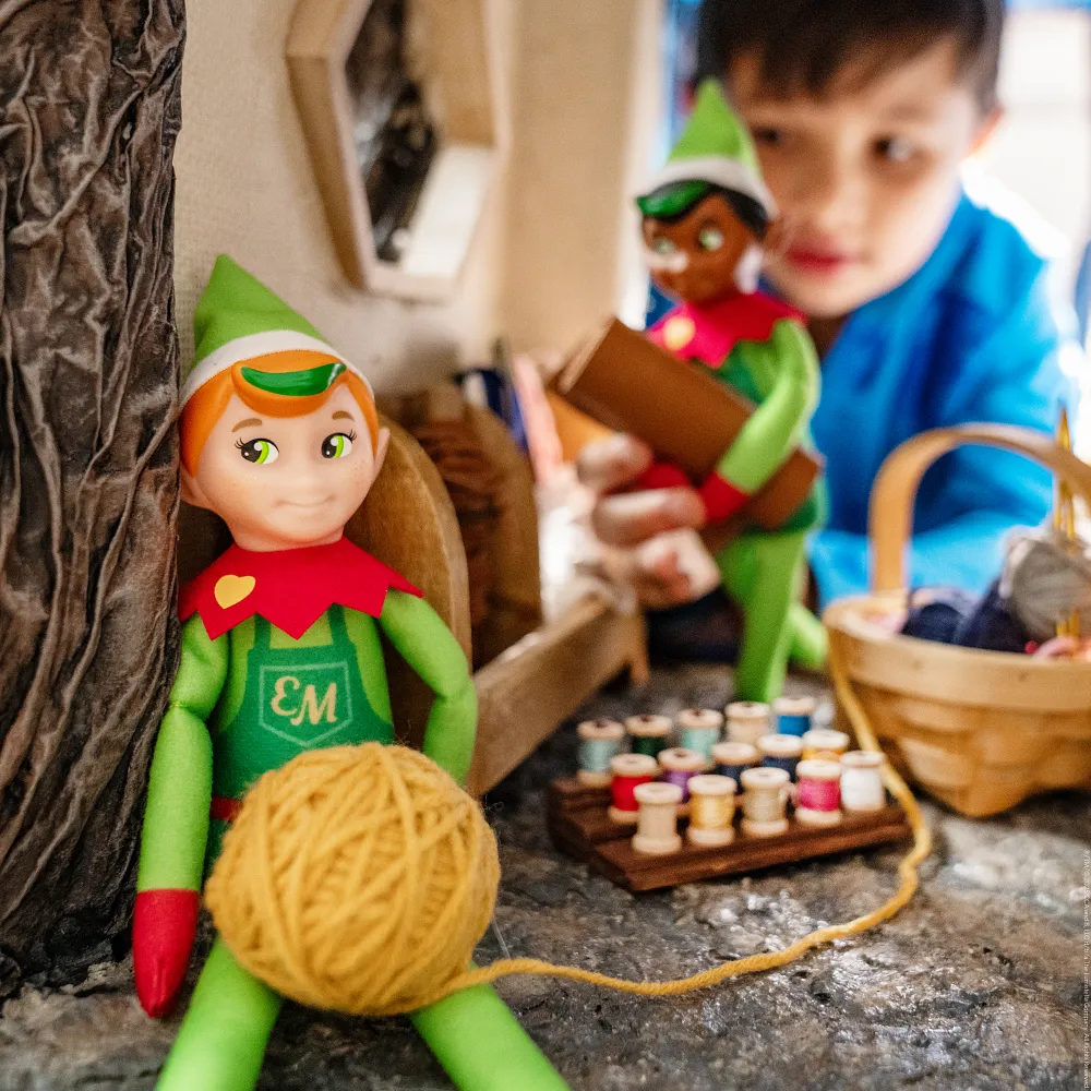Child playing with Elf Mates dolls in a dollhouse scene with yarn, sewing props and imaginative kindness play