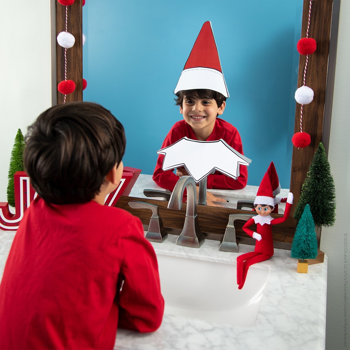A child looks into a mirror where a paper Scout Elf hat and collar frame their reflection.