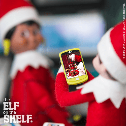 Two Scout Elves hold a phone showing Santa on the screen during a video call.