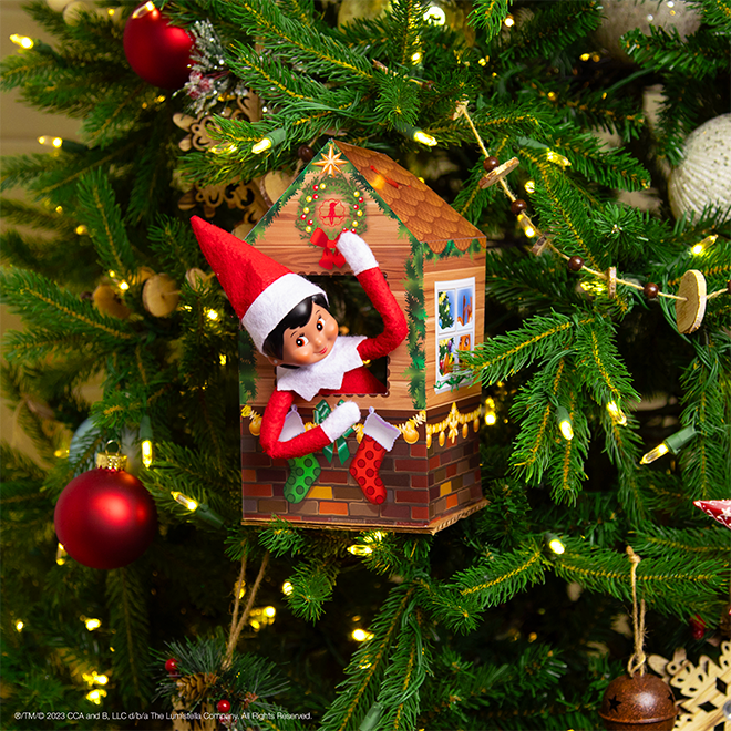 A Scout Elf sits in a paper tree house tucked among the branches of a decorated Christmas tree.