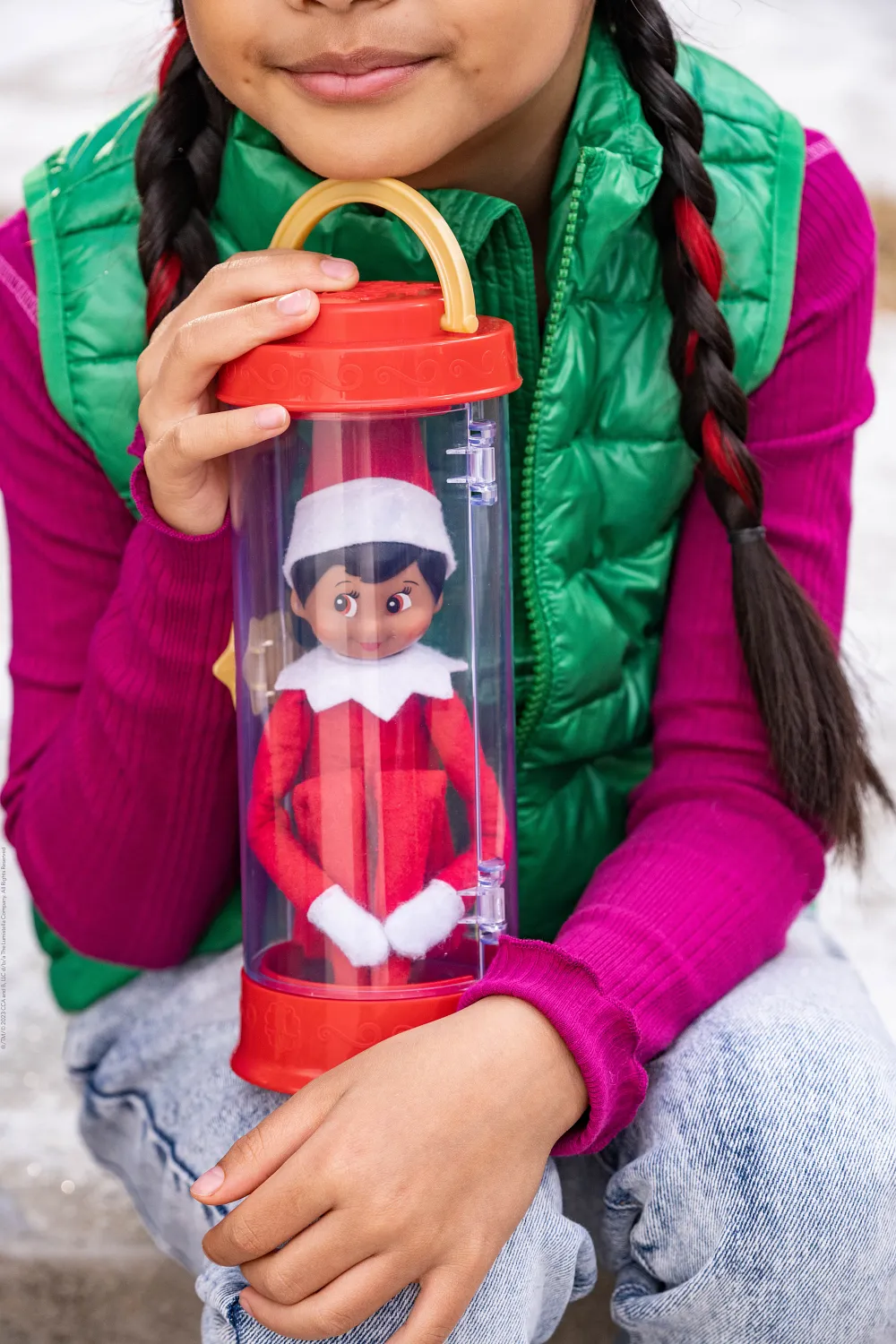 A smiling girl in a green gilet holding a Scout Elf safely inside a clear Scout Elf Carrier